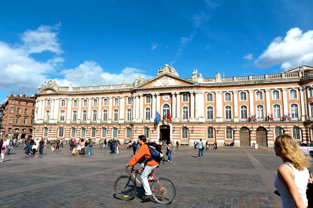 place du capitole à Toulouse sous le soleil avec des piétons et cyclistes.
