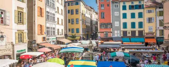 La très animée place du Plot, avec ses façades colorées et son marché, au Puy-en-Velay.