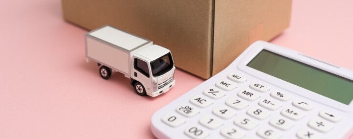 calculatrice à côté d'un camion miniature et d'un carton de déménagement, sur fond rose