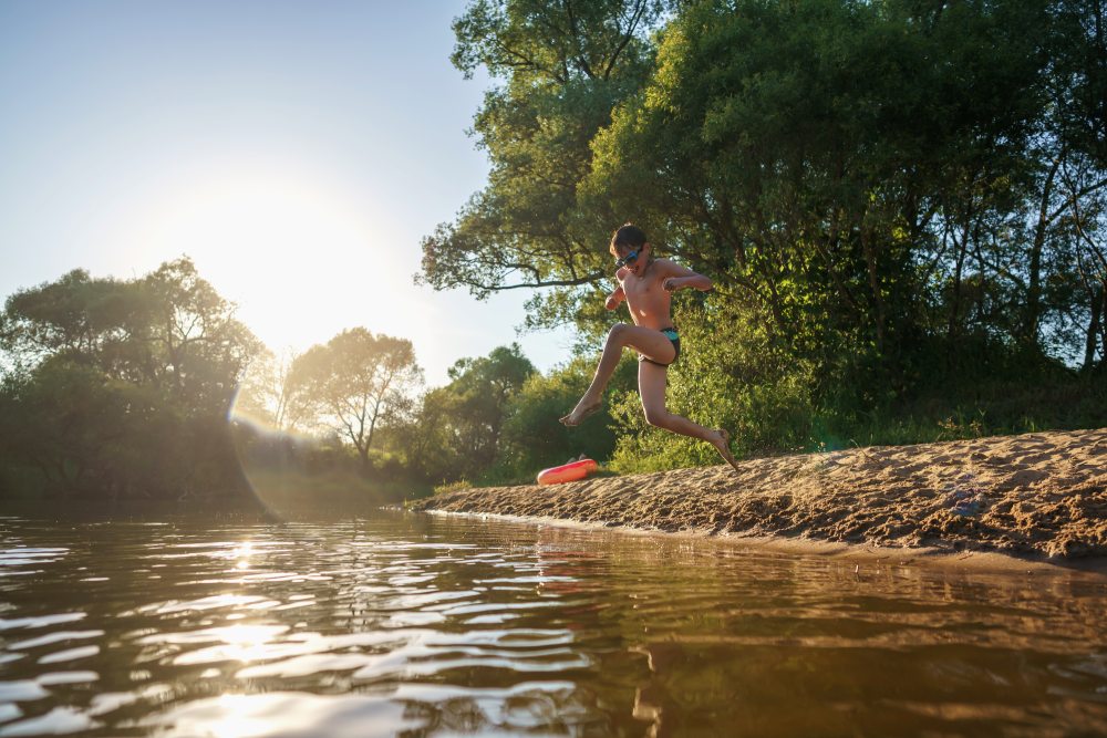 un enfant qui saute dans une rivière entourée d'arbres