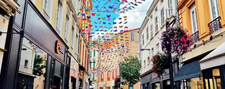 Vue de la rue du Maréchal Foch à Roanne, un jour ensoleillé, avec des guirlandes de papillons suspendues.