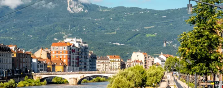 Vue de Grenoble avec une piste cyclable au bord de la rivière, des montagnes en arrière-plan.