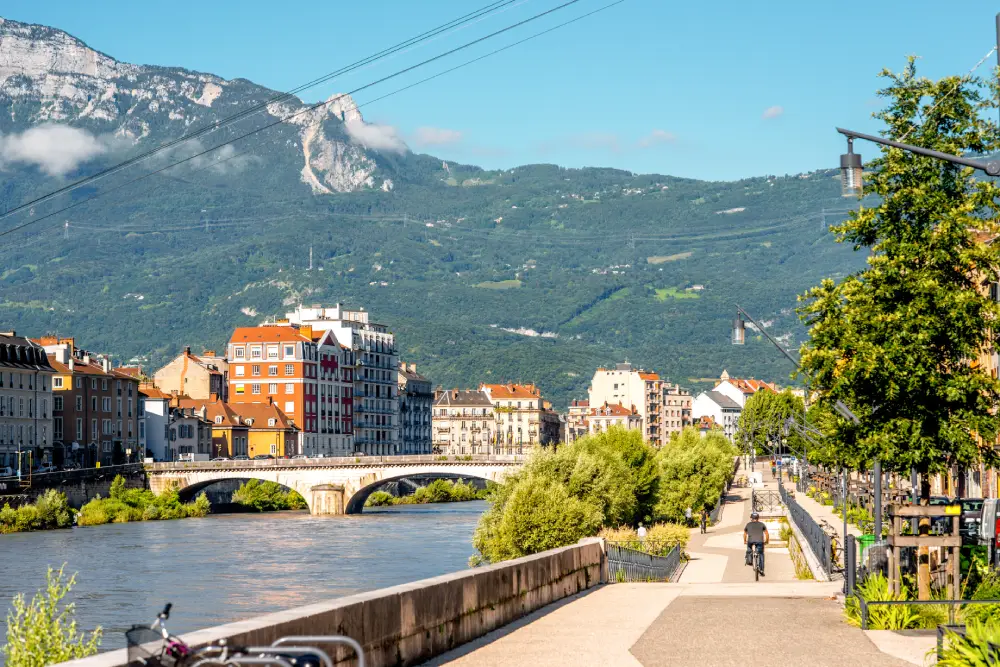 Vue de Grenoble avec une piste cyclable au bord de la rivière, des montagnes en arrière-plan.