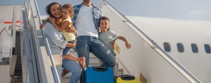 famille heureuse en train de descendre d'un avion avec deux enfants et des petites valises.