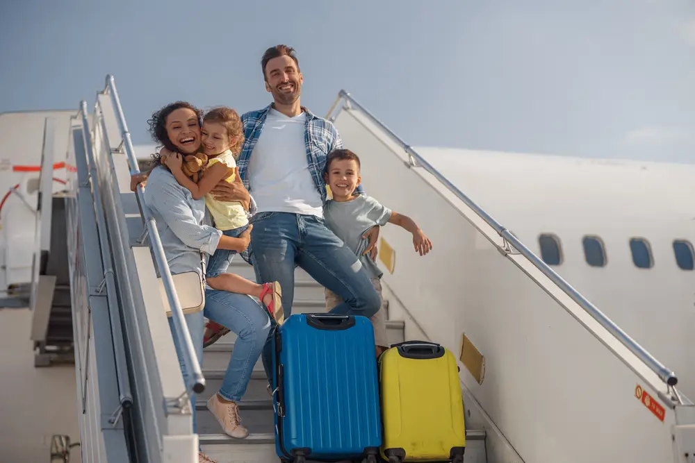 famille heureuse en train de descendre d'un avion avec deux enfants et des petites valises.