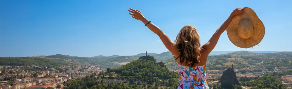 Femme de dos devant une vue de la ville du Puy en Velay, l'été